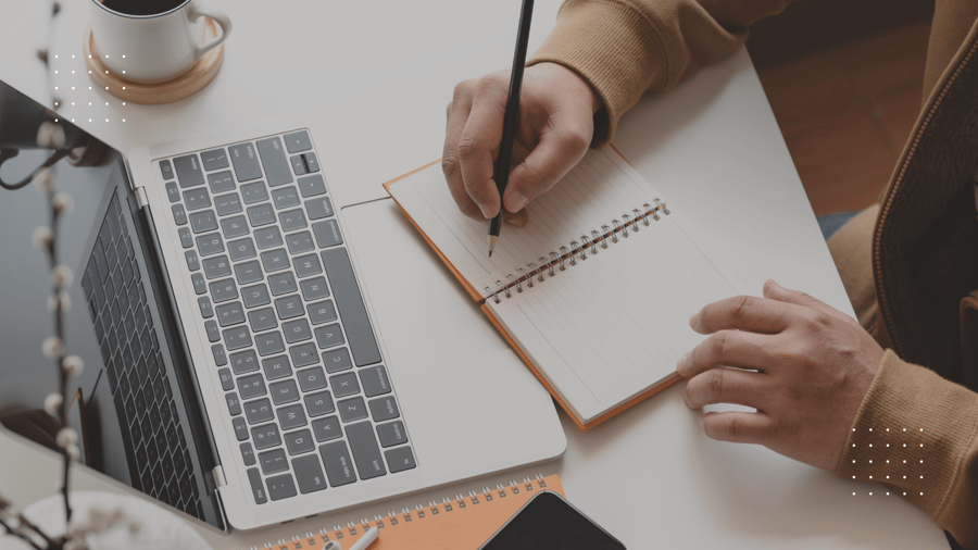 hands taking notes on paper in front of laptop screen